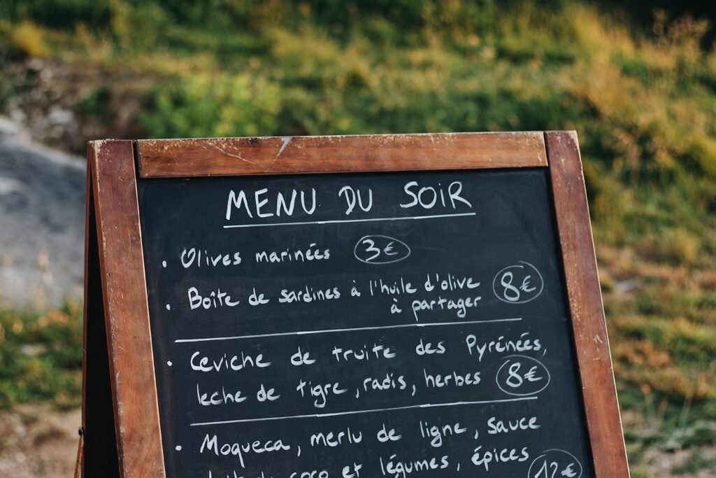 Chalkboard menu stand listing French dishes and prices in an outdoor setting.